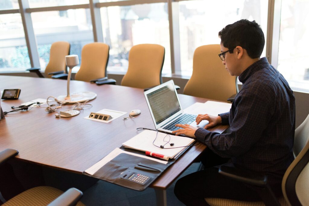 A man using a laptop at a modern conference room table during a meeting, showcasing a professional workspace setup with conference room tables.